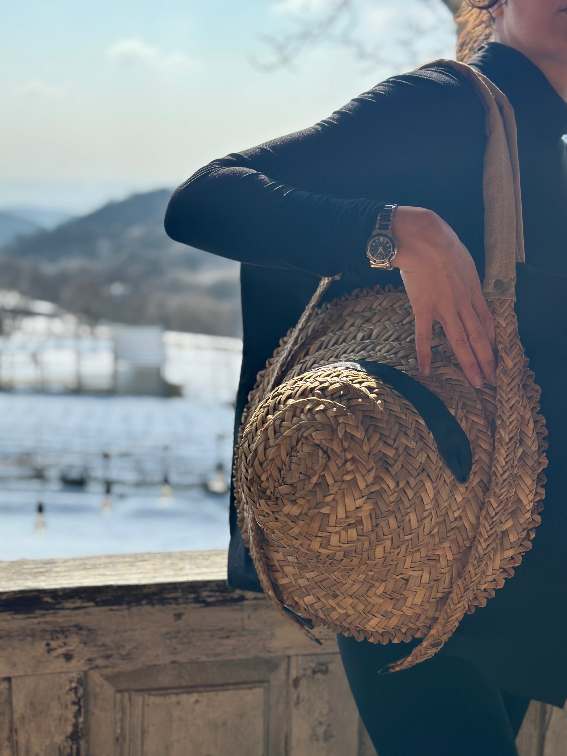 Black tote bag with straw handles for carrying a hat